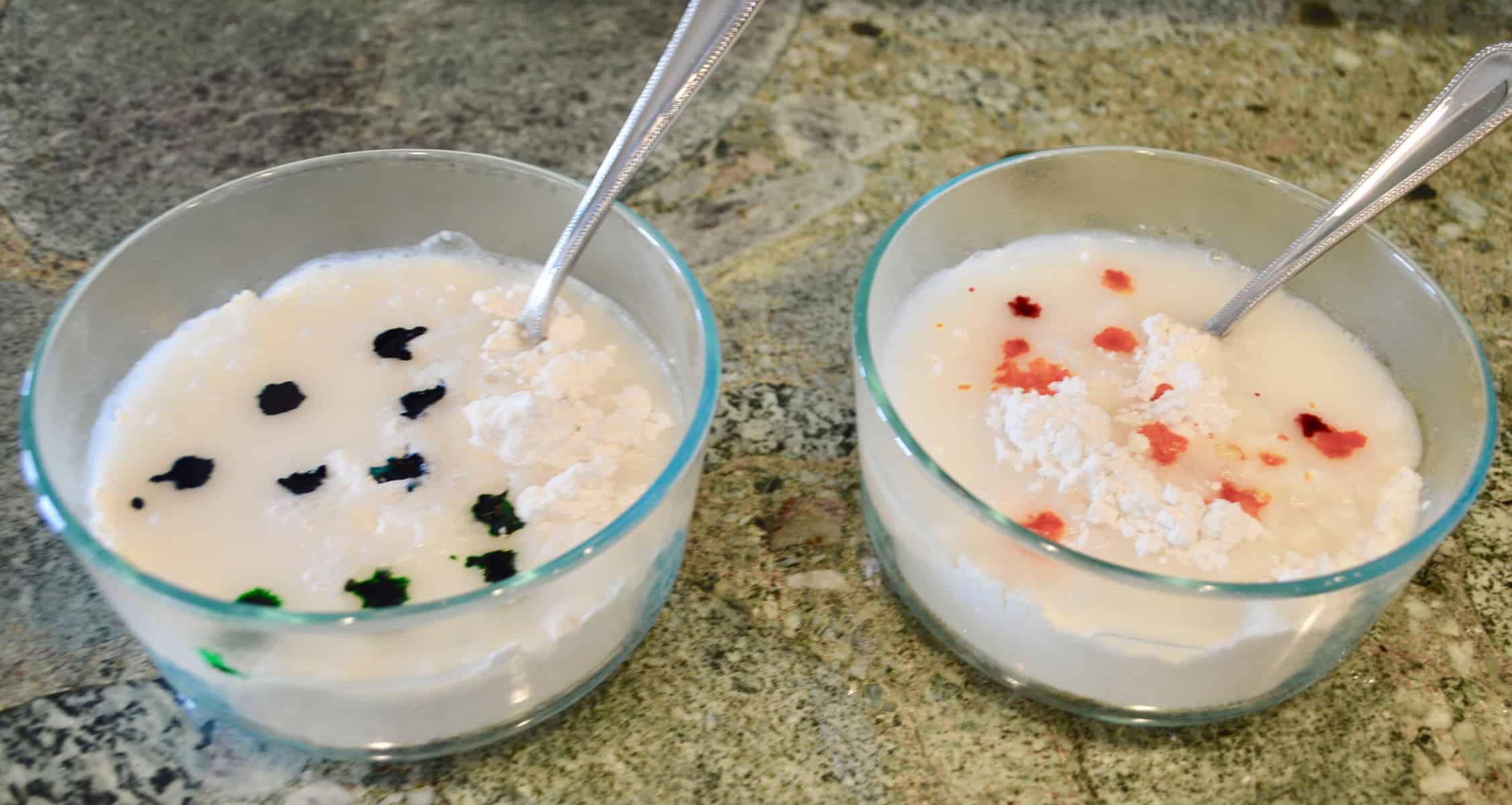 Two bowls of water and flour with food coloring drops on a countertop 