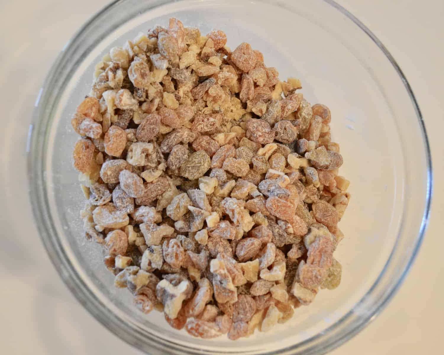 Raisin and walnuts tossed in flour in a glass bowl on a white countertop 