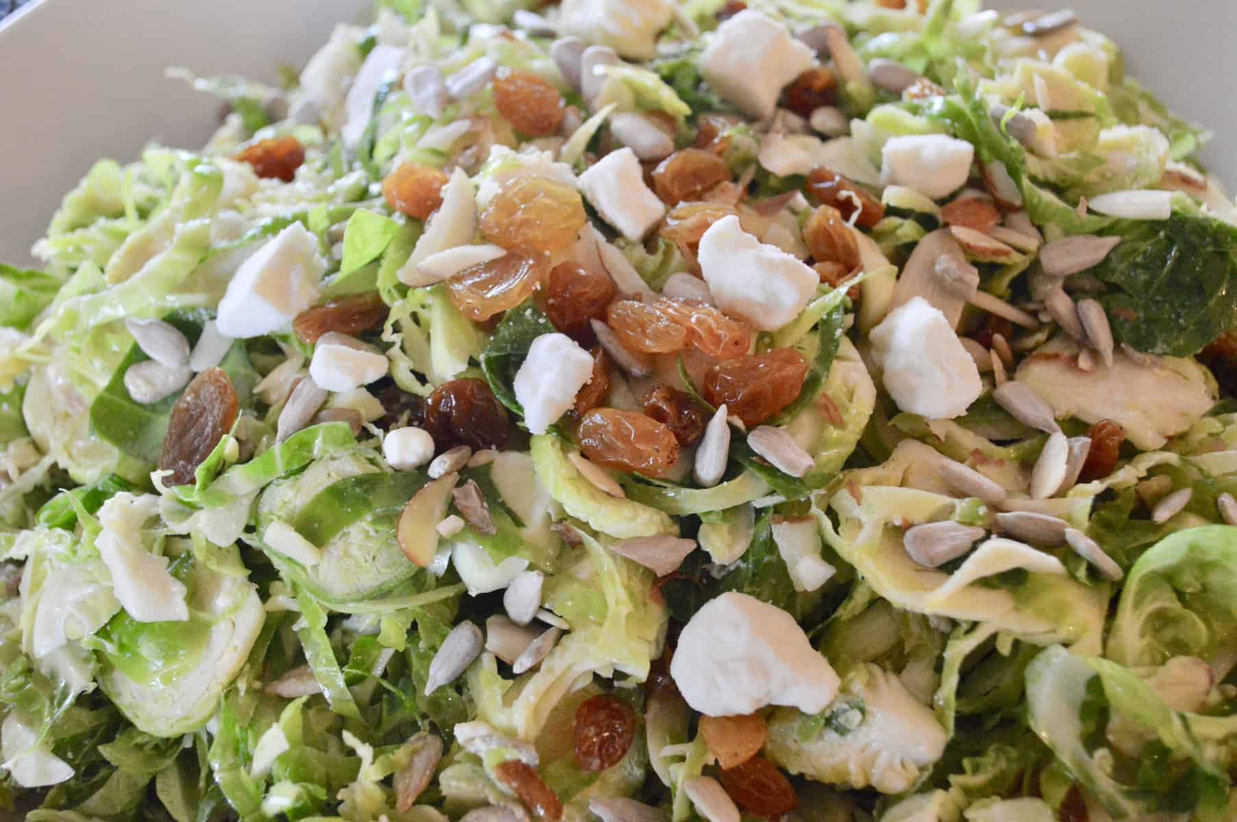 Brussels sprouts Salad with feta raisins and almonds in white bowl