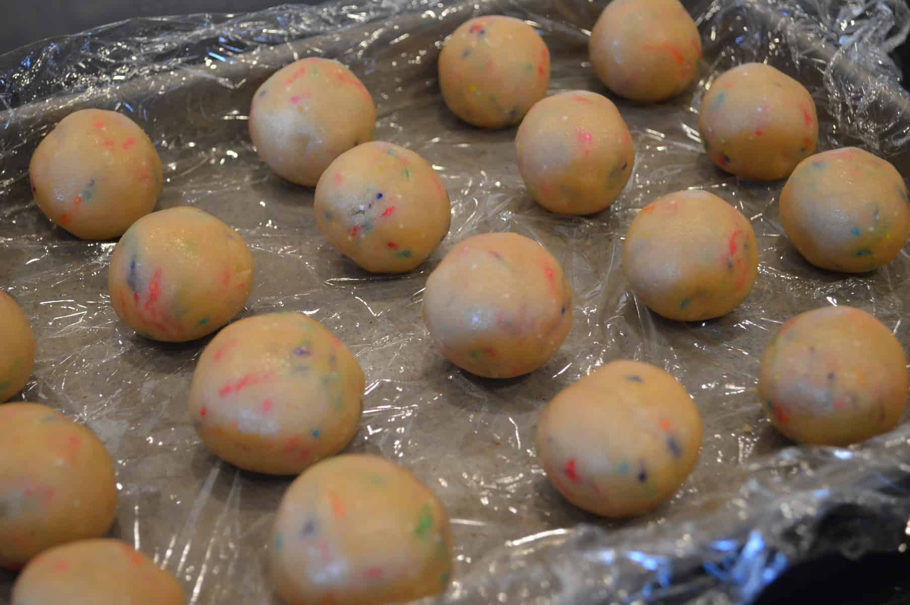 cake pop batter rolled into balls on a plastic lined baking sheet. 