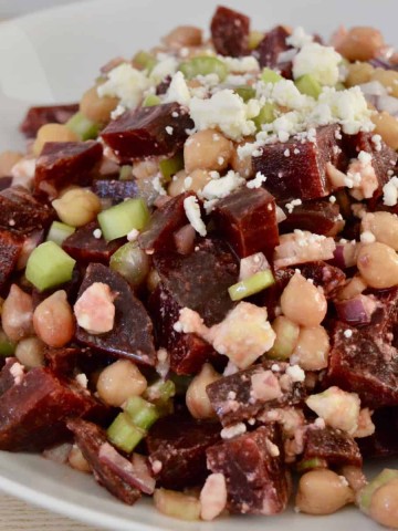 Beet salad with garbanzo beans, feta, celery, and red onion in a white serving bowl.