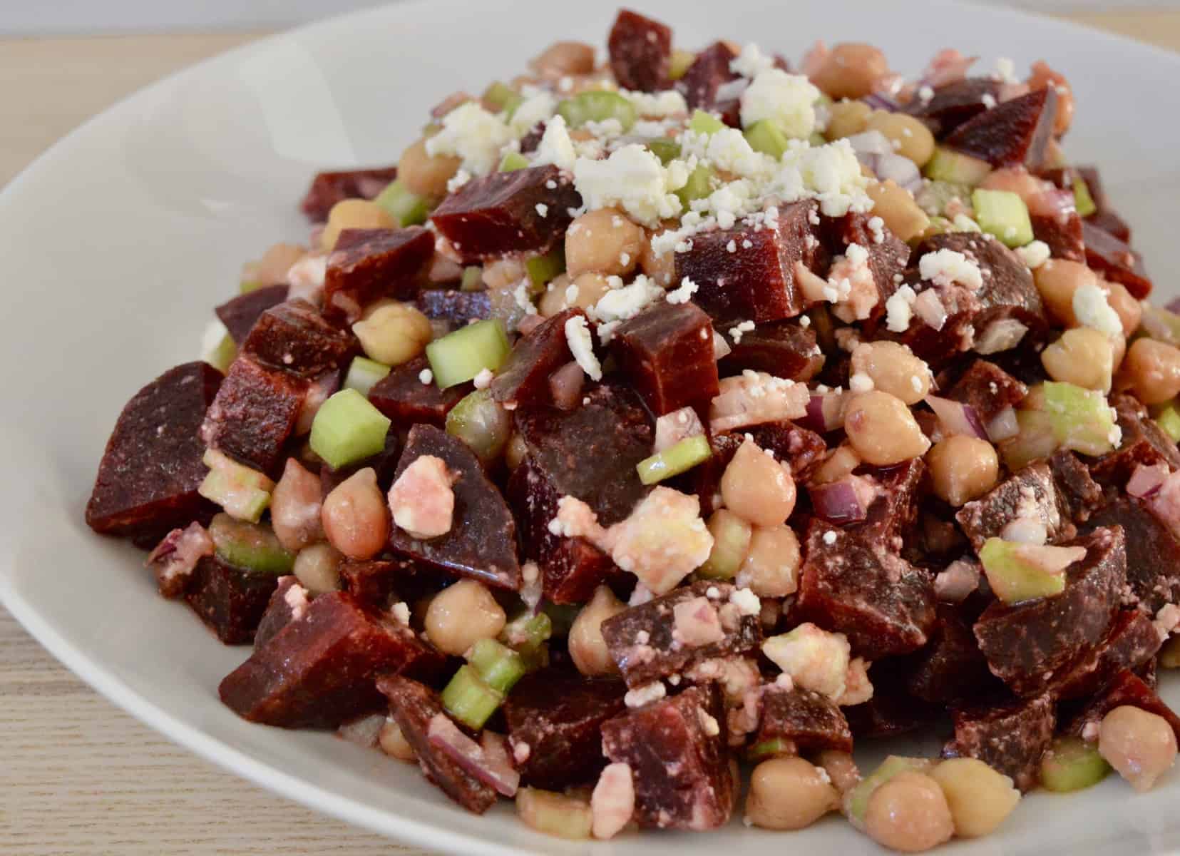 Beet salad with garbanzo beans, feta, celery, and red onion in a white serving bowl. 