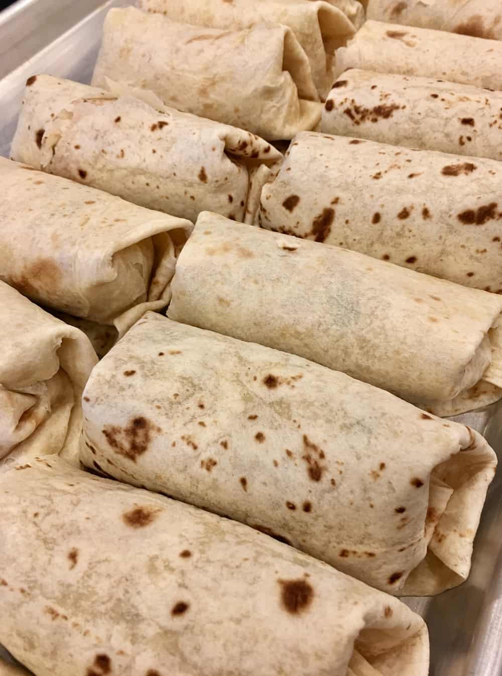 tray full of rolled tortillas with filling. 