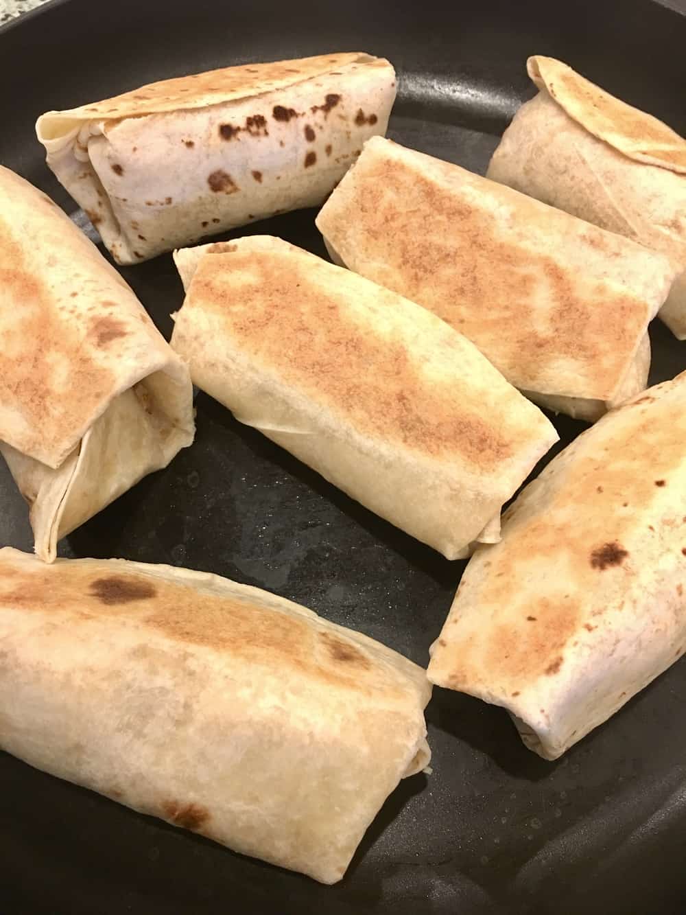 burritos on a saute pan getting sealed.