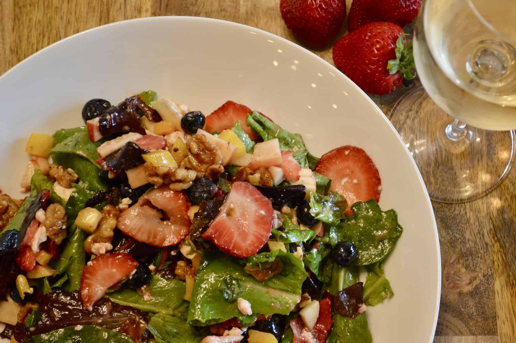 berry salad with candied walnuts on a wood table with a wine glass and strawberries 