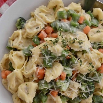 tortellini with veggies and parmesan cheese on top in a white bowl.