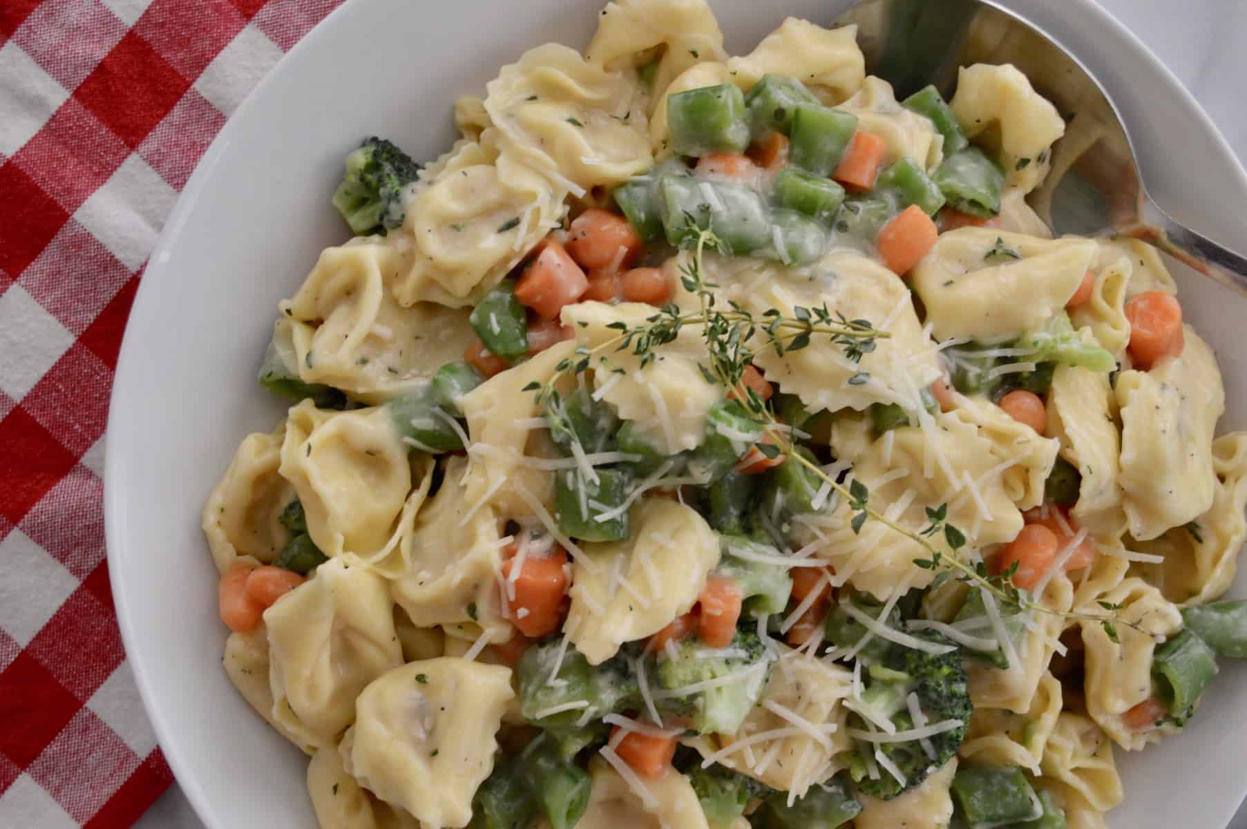 tortellini with veggies and parmesan cheese on top in a white bowl. 