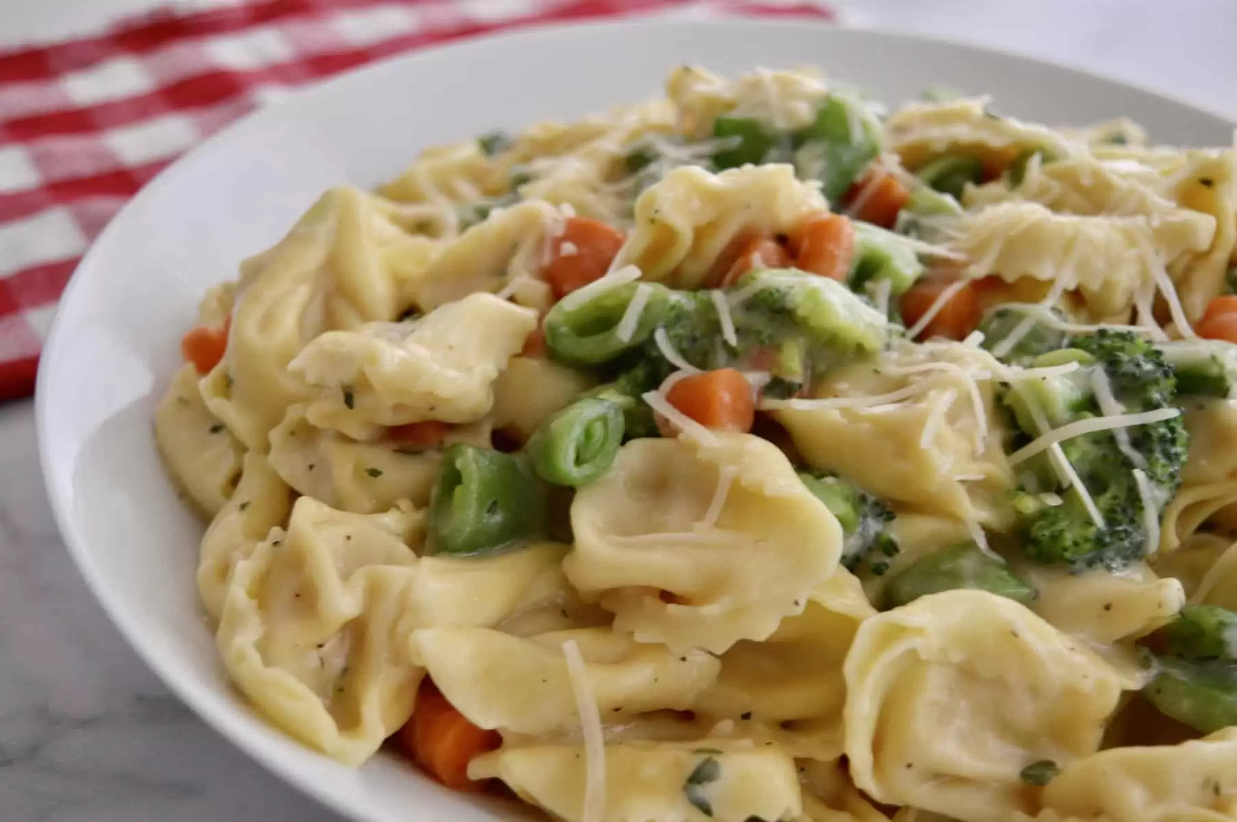 close up of tortellini with carrots, peas, and broccoli in a white plate. 