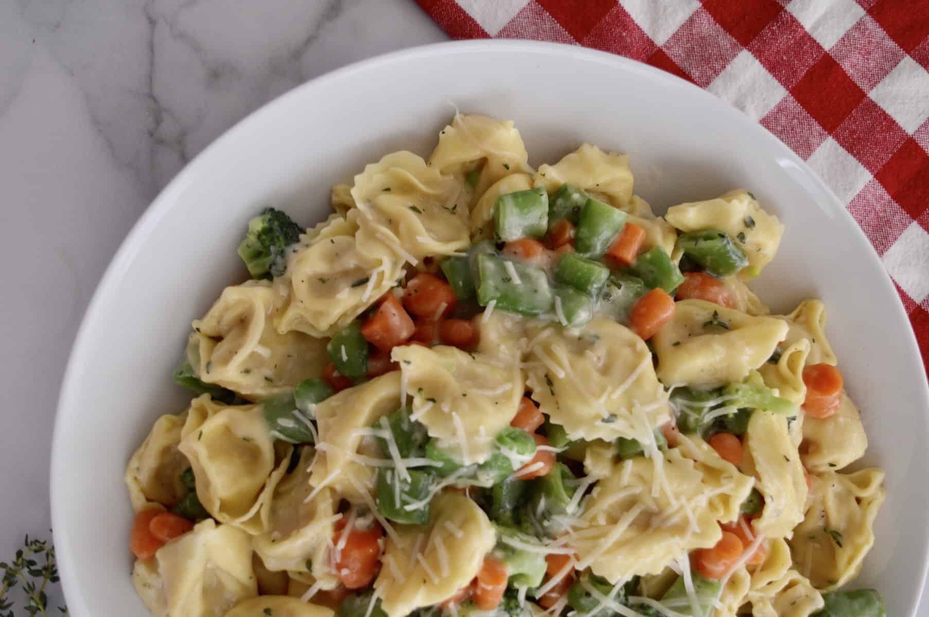 tortellini primavera in a white dish with a checkered napkin in the background. 