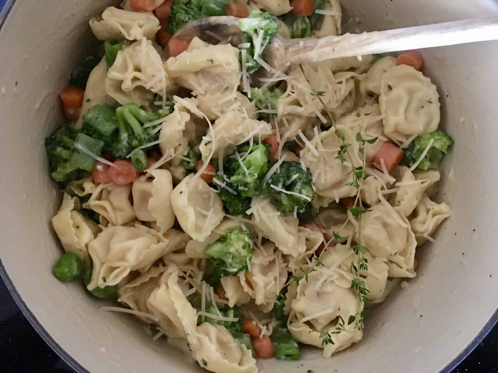 pot of tortellini primavera with a wooden spoon in it. 