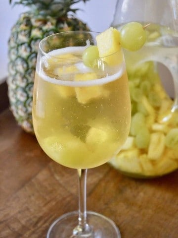 Tropical White wine spritzer in a glass with pineapple and grapes and a pineapple in the background