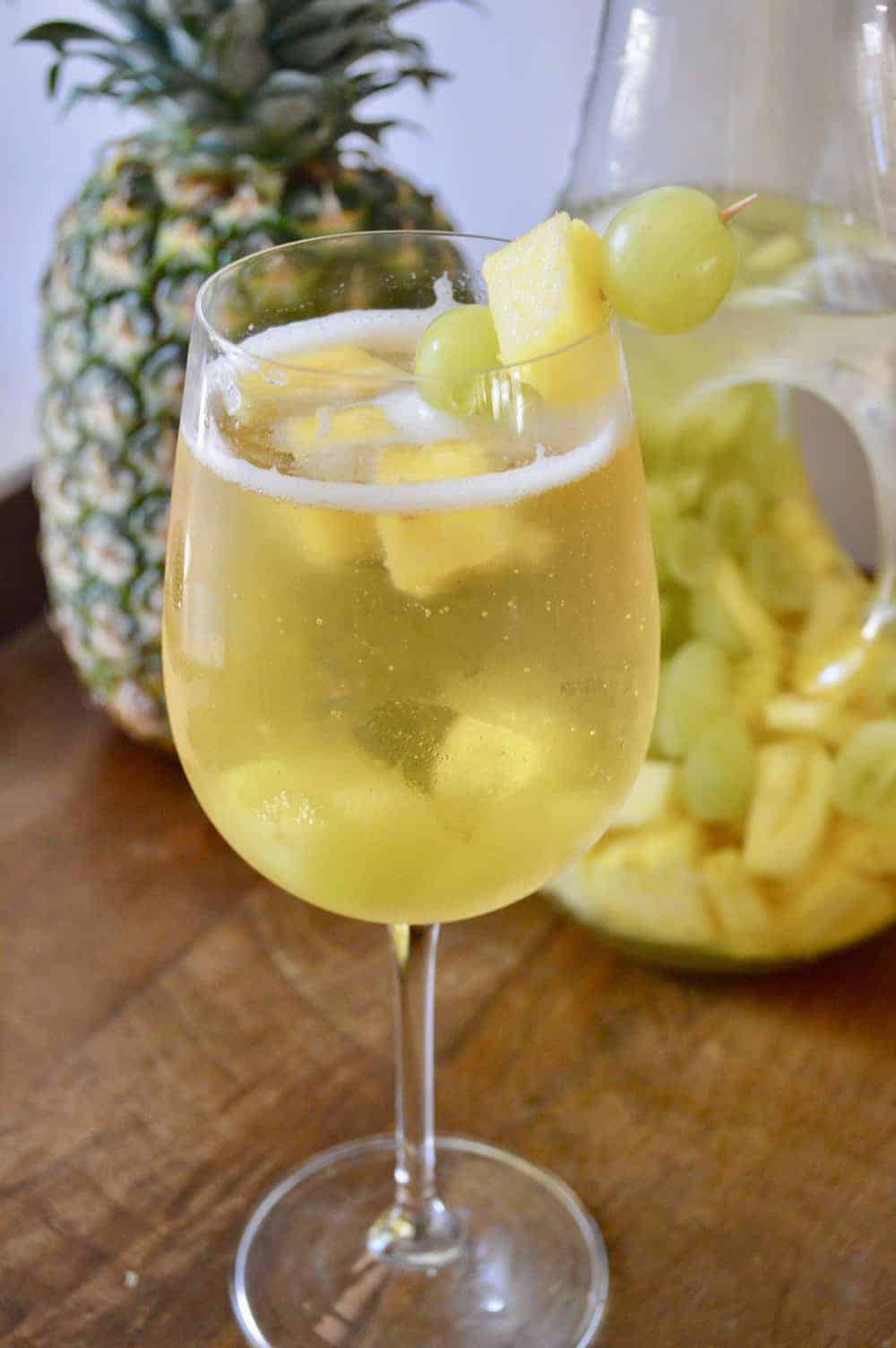 Tropical White Wine Spritzer in a wine glass with pineapple and grapes and a pineapple in the background 