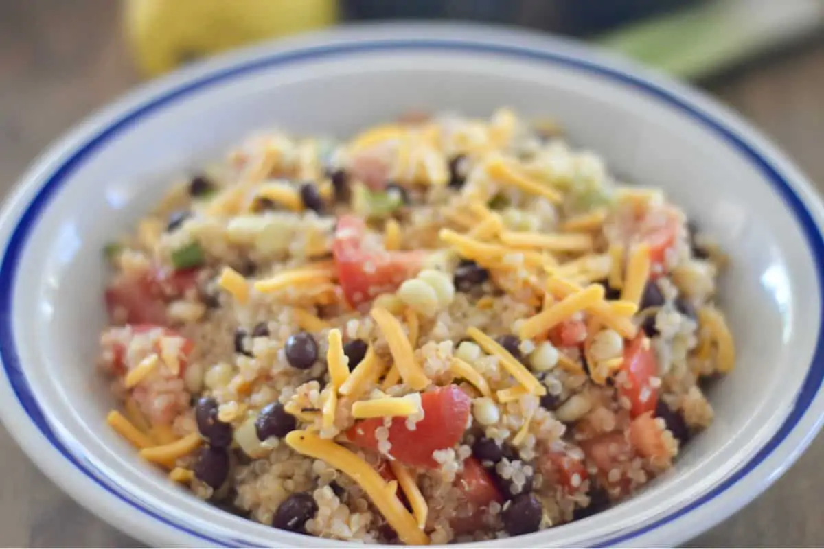 White bowl with a blue trim holding the recipe topped with shredded cheddar cheese. 