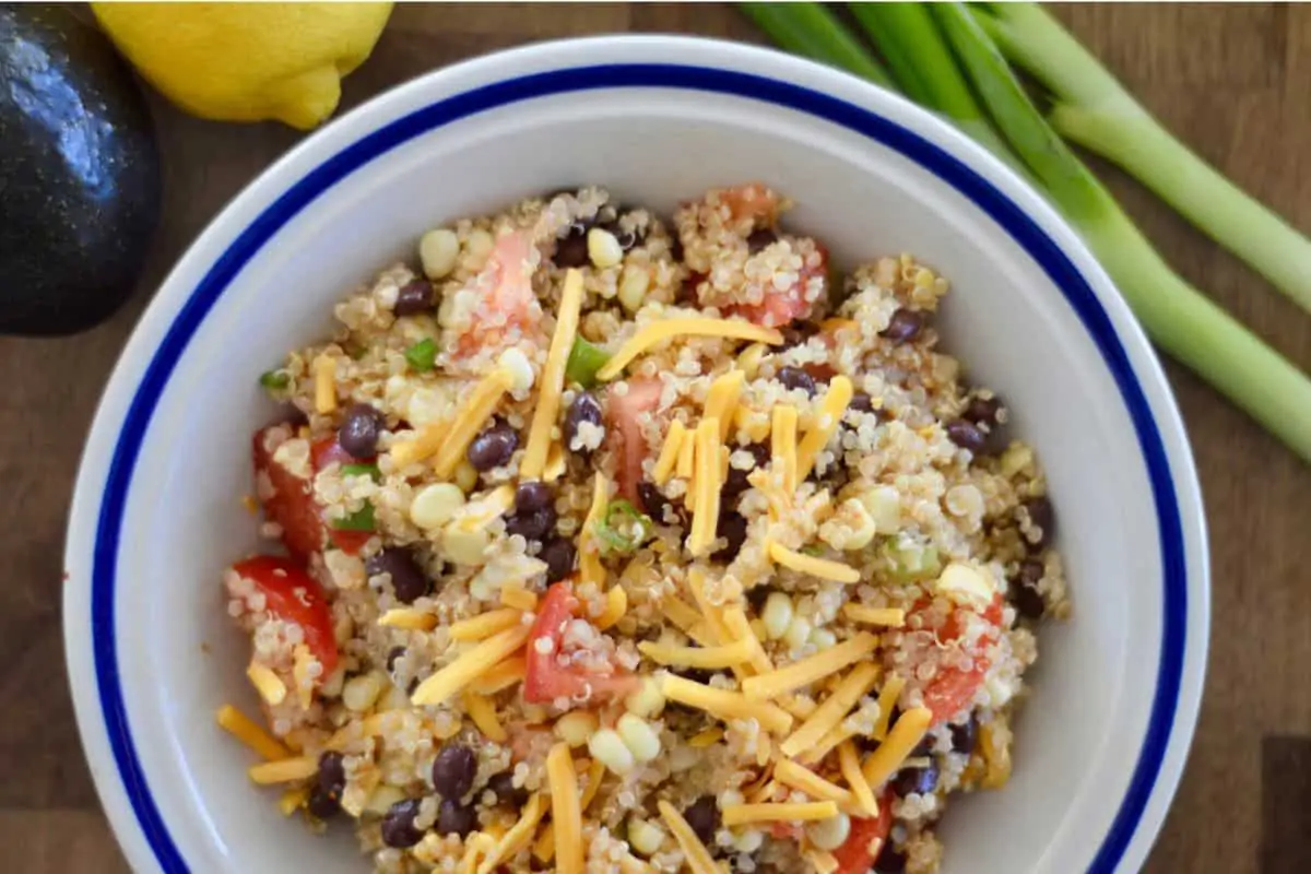 Mexican Quinoa salad with black beans, corn, and shredded cheddar cheese in a white bowl. 