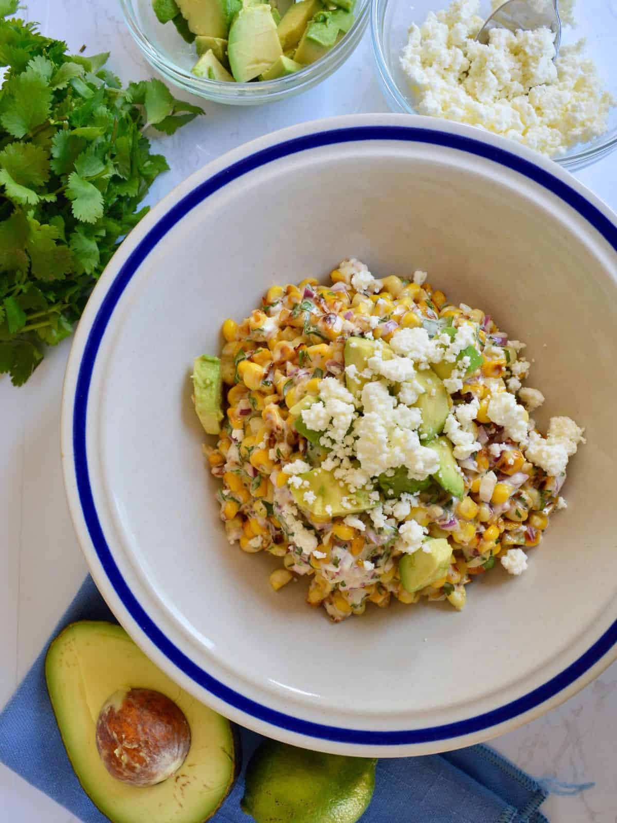 Mexican street corn with avocado in a white bowl. 