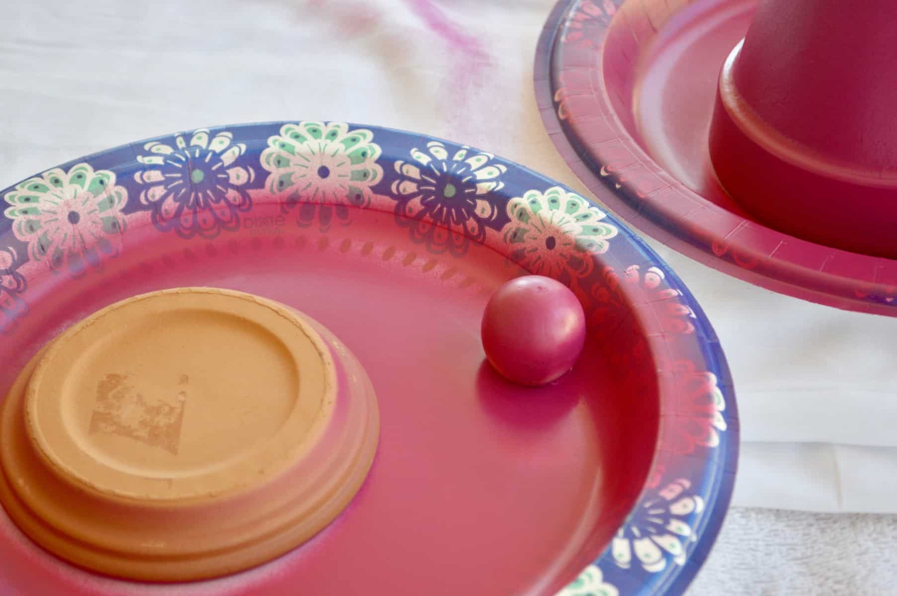 spray paint the wooden doll heads on a paper plate with magenta spray paint