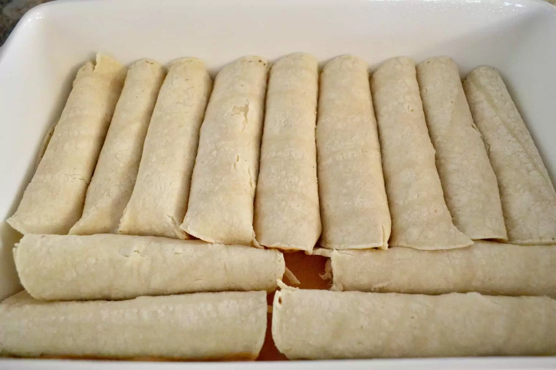 rolled enchiladas in a baking pan of sauce for cream cheese chicken enchiladas