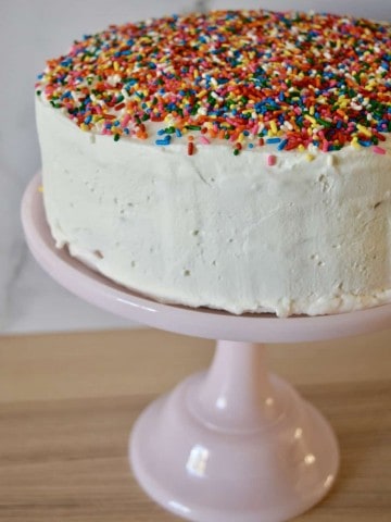 Ice Cream Cake with sprinkles on top sitting on a pastel pink pedestal.