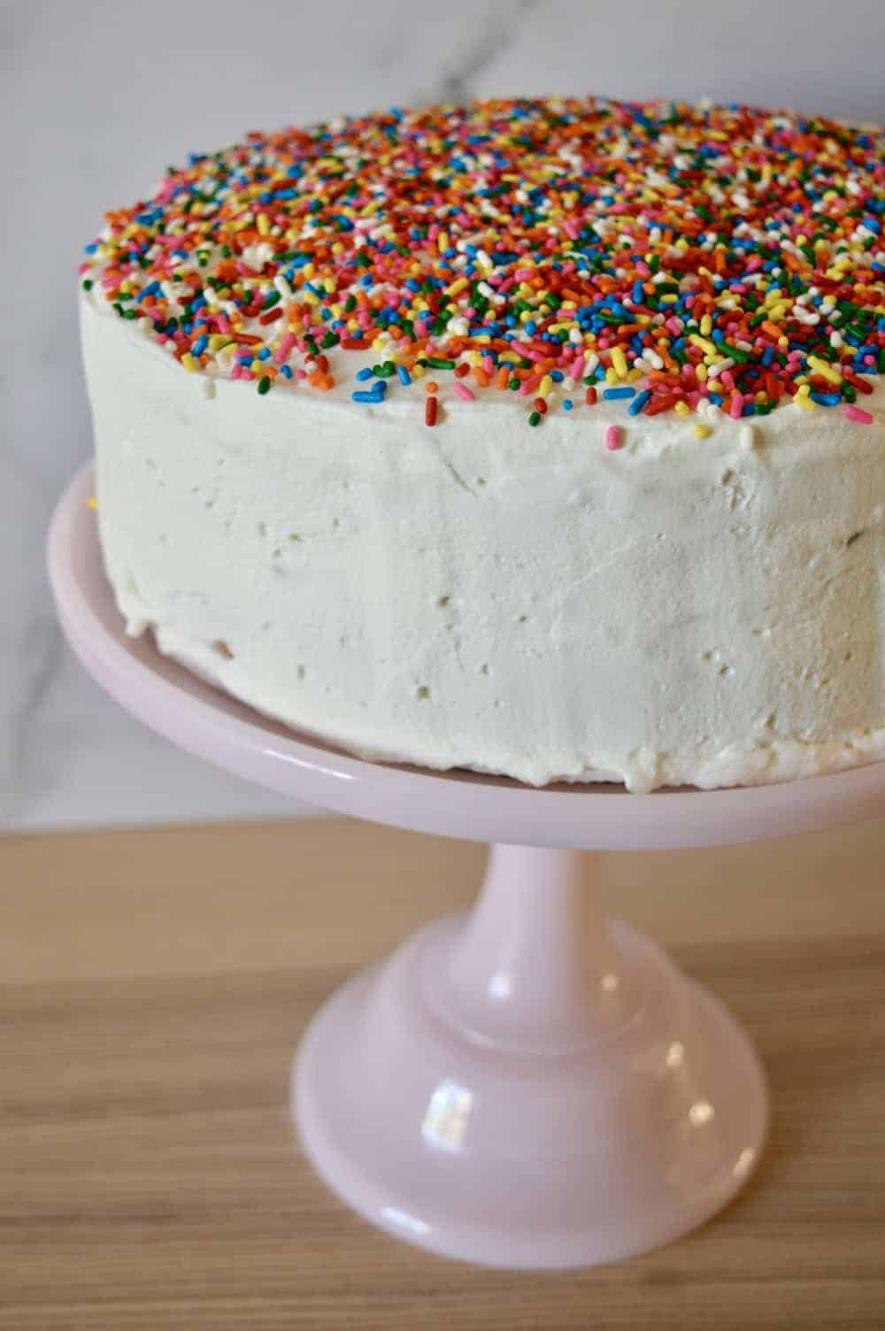 Ice Cream Cake with sprinkles on top sitting on a pastel pink pedestal. 