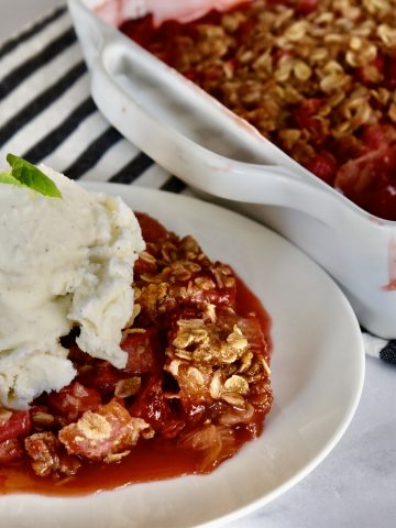 Strawberry Rhubarb Crisp on a white plate with ice cream on top.