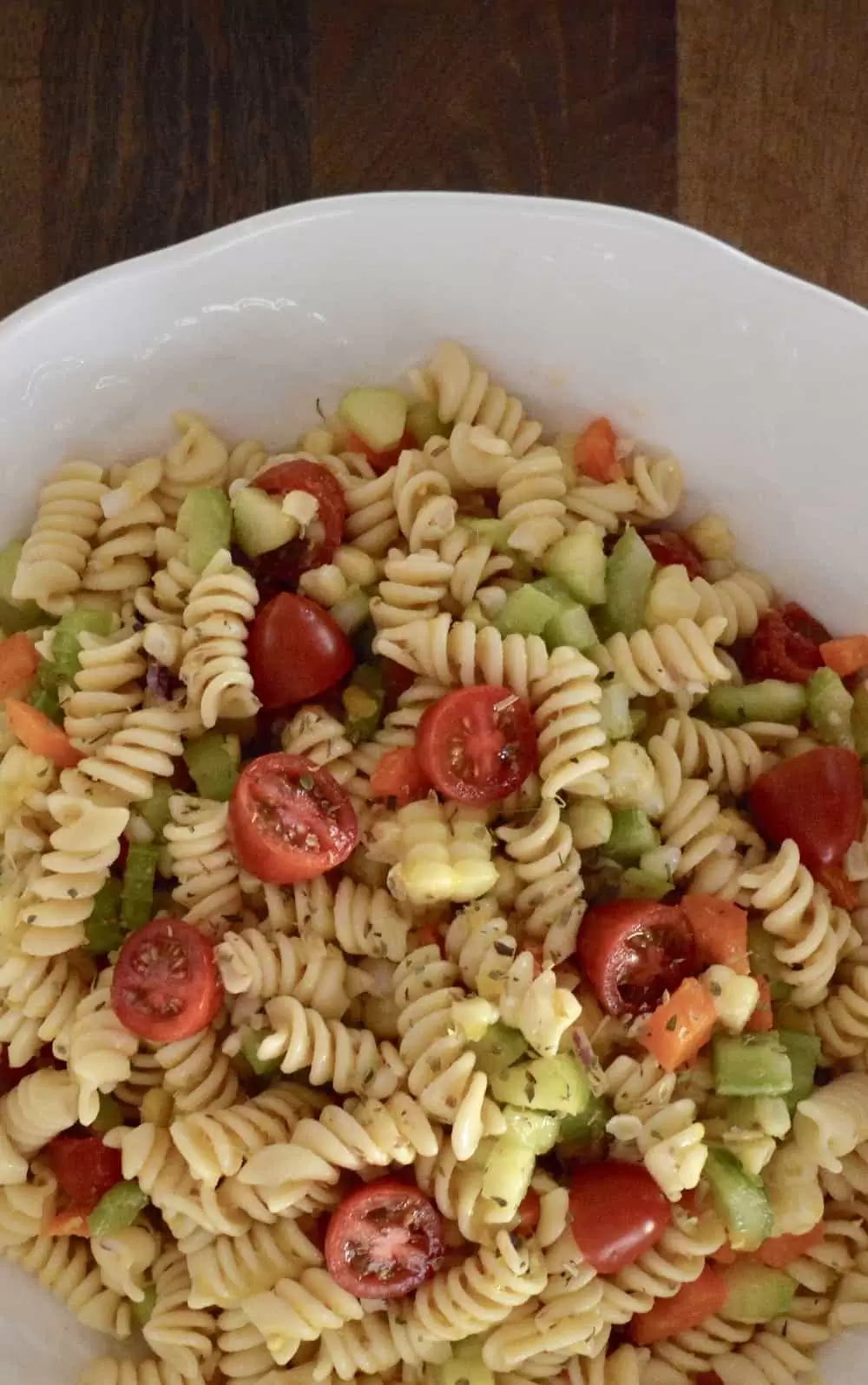 pasta salad with lots of vegetable and corn in a white bowl on a wood surface