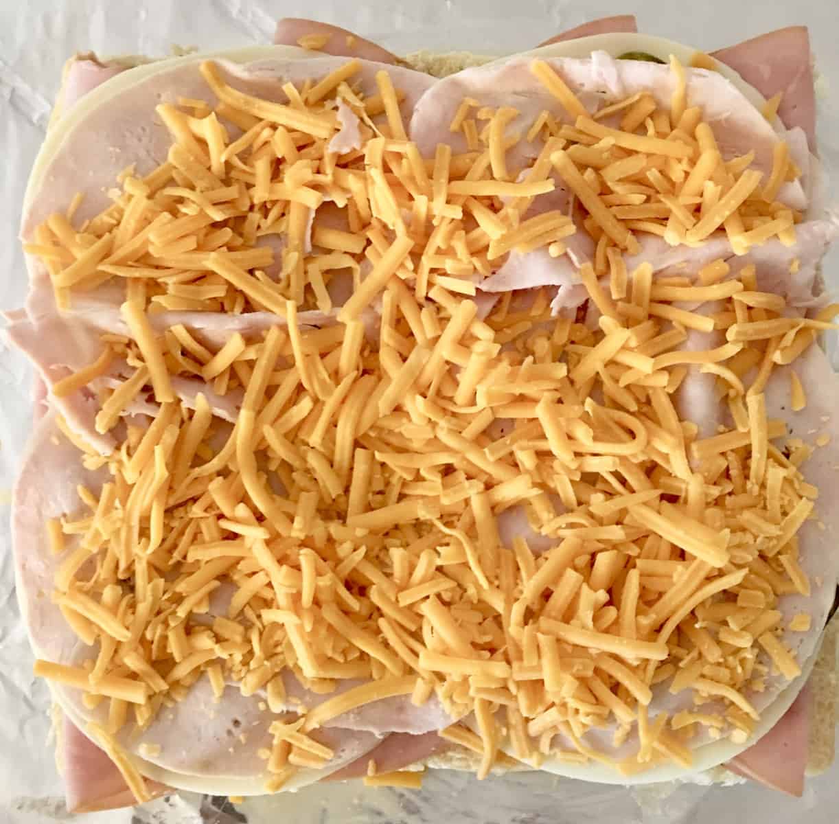 add the shredded cheddar cheese to the ham and cheese sliders 