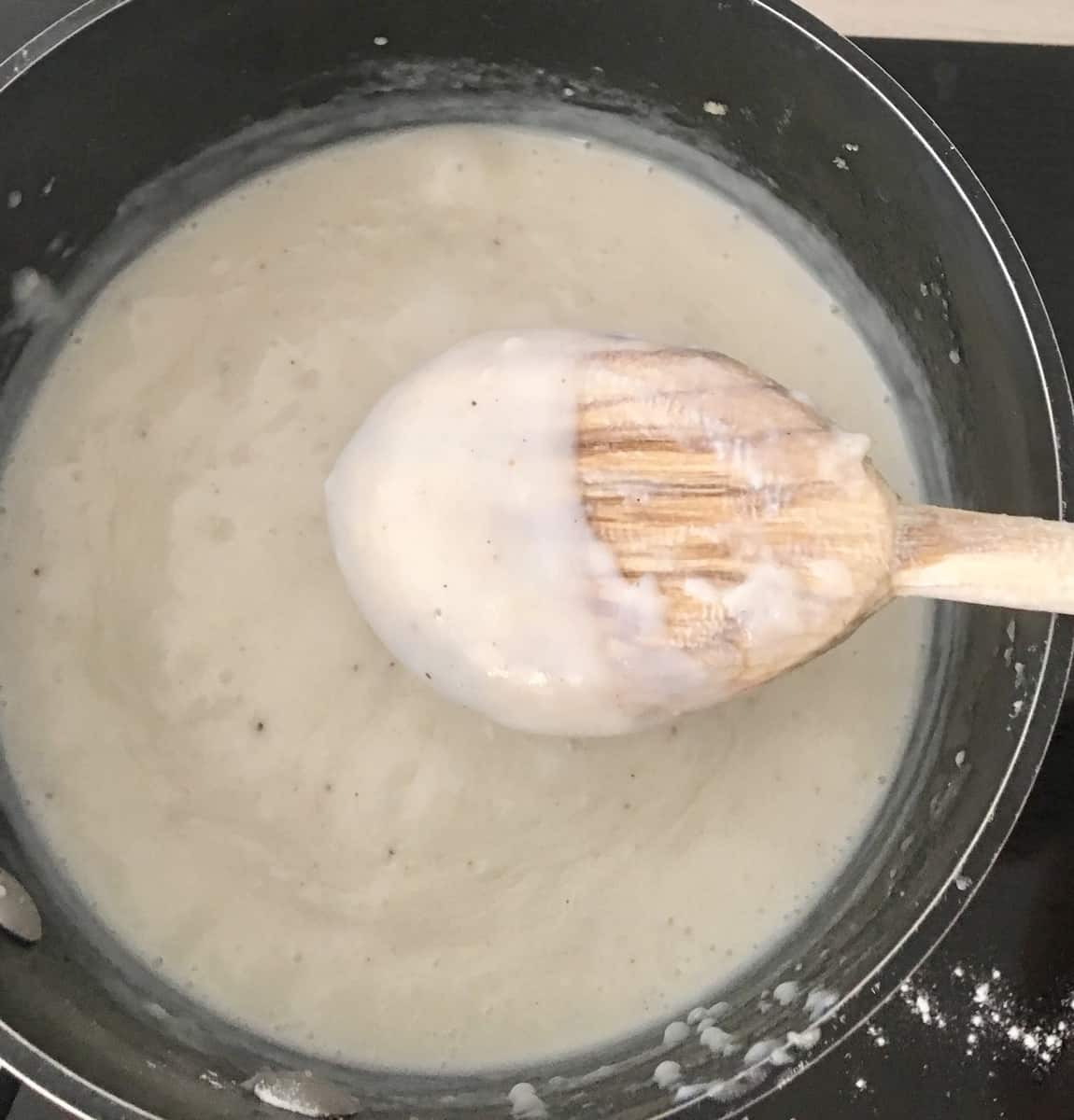 bechamel sauce on the stove with a wooden spoon. 
