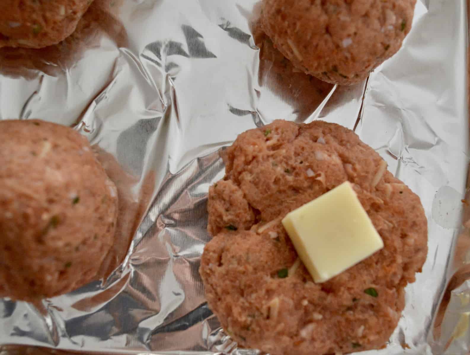 meat with a piece of cheese in the middle on a foil baking pan. 