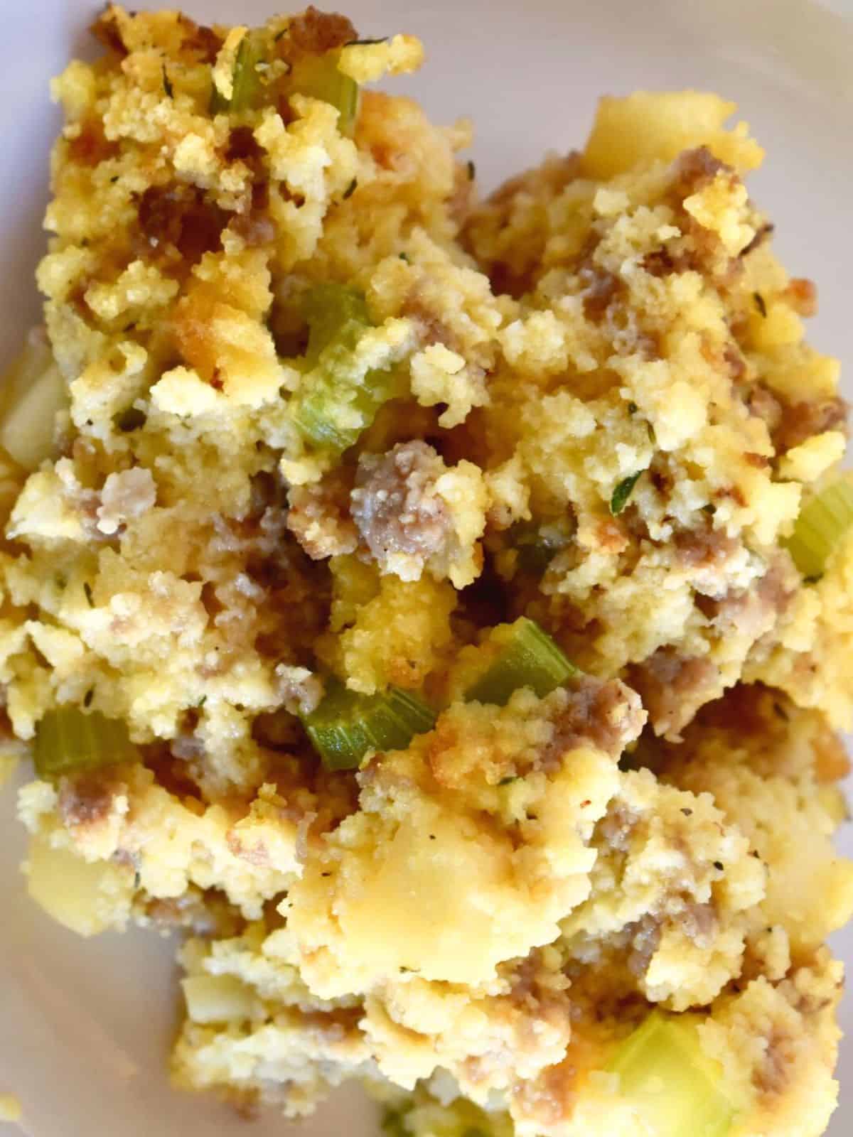 Fluffy cornbread stuffing with sausage and apples on a white plate. 