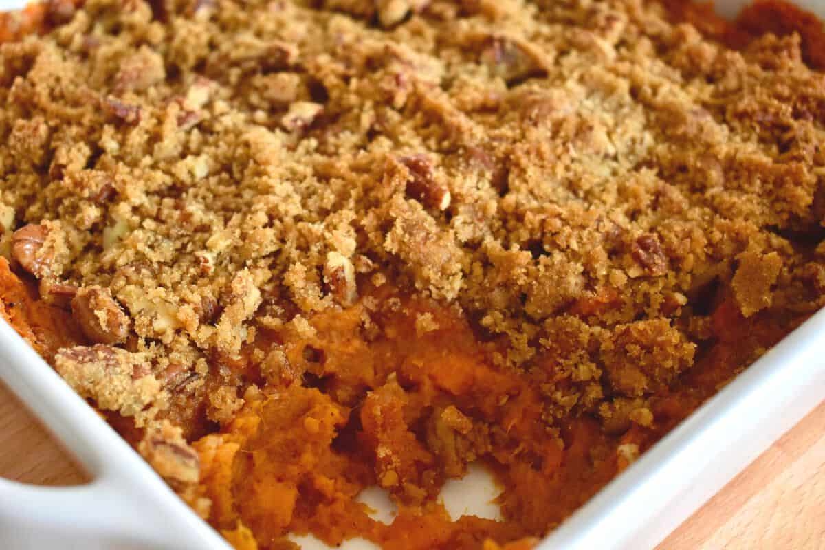 Sweet Potato Casserole with pecan streusel topping in a white dish with a scoop out of it. 