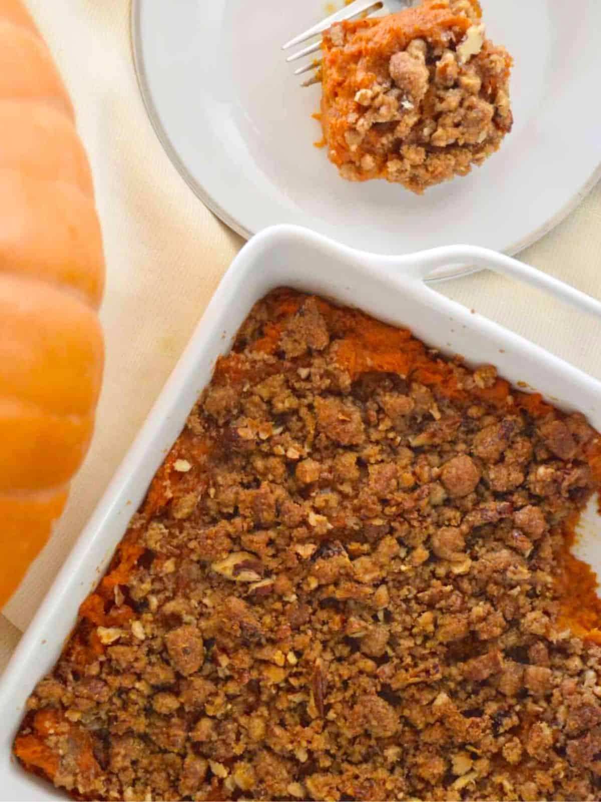 Sweet Potato Casserole with pecan streusel topping on a table with a pumpkin next to it. 