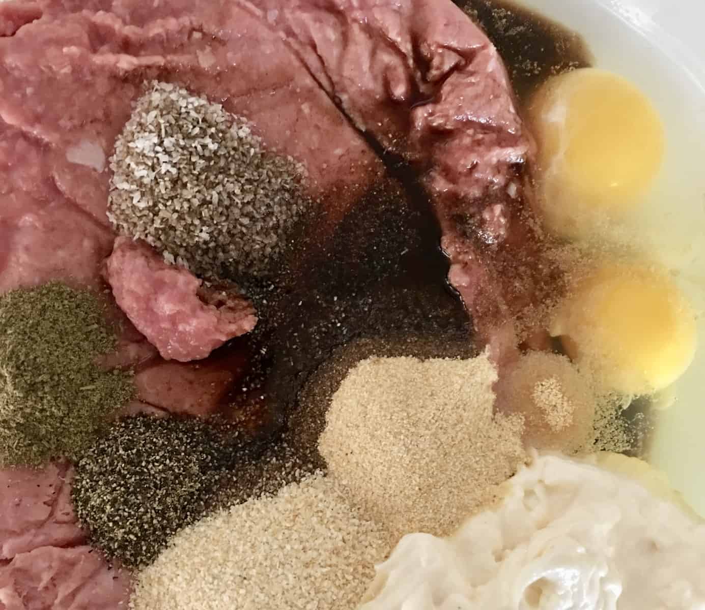 ground meat, eggs, pepper, and other ingredients in a bowl. 