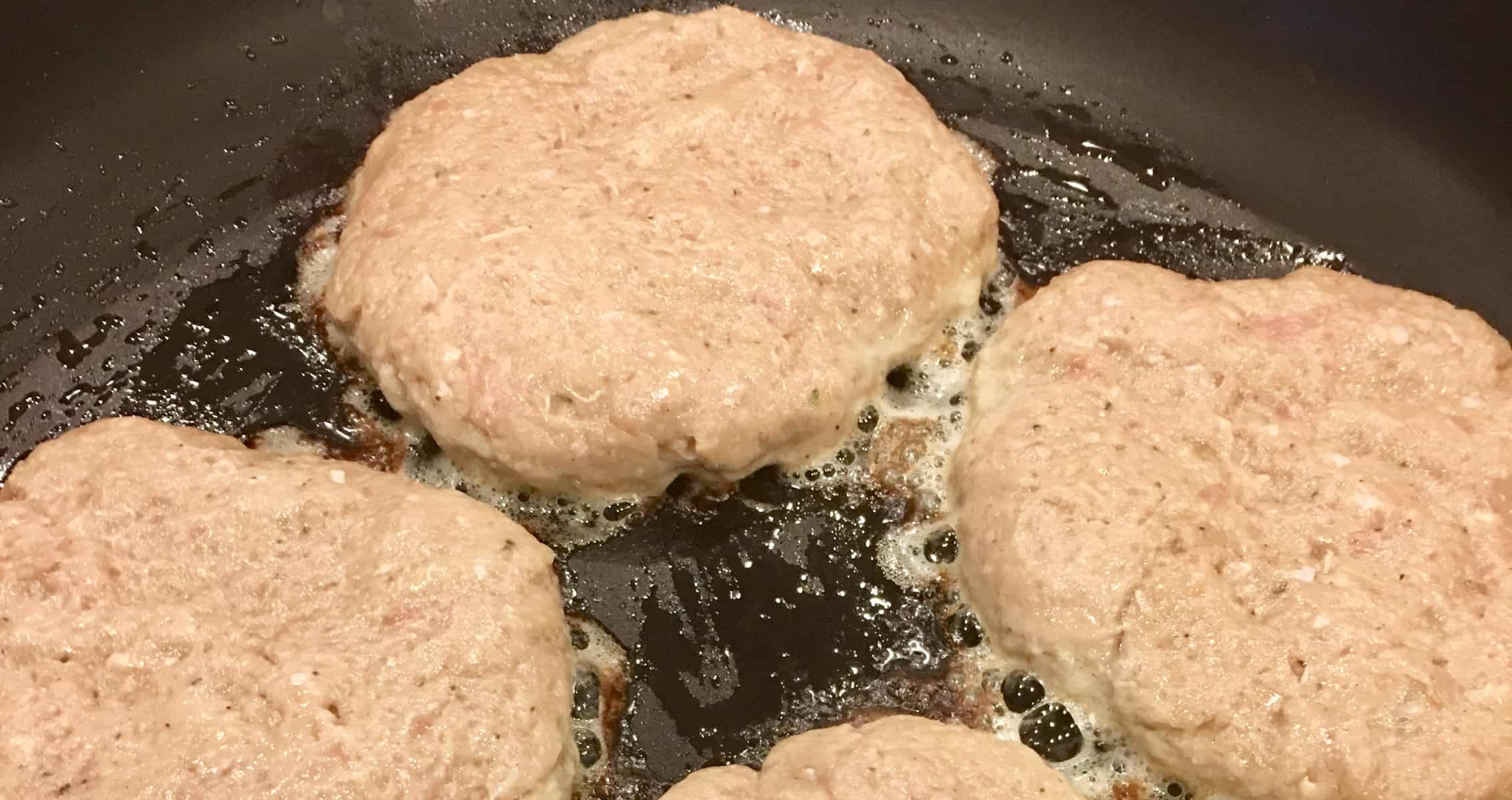 meat patties frying in a black frying pan. 