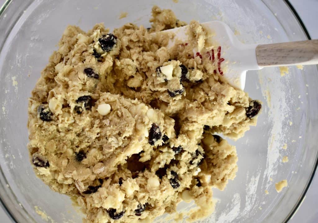 overhead photo of white chocolate cranberry cookie batter in a glass bowl with spatula in it. 