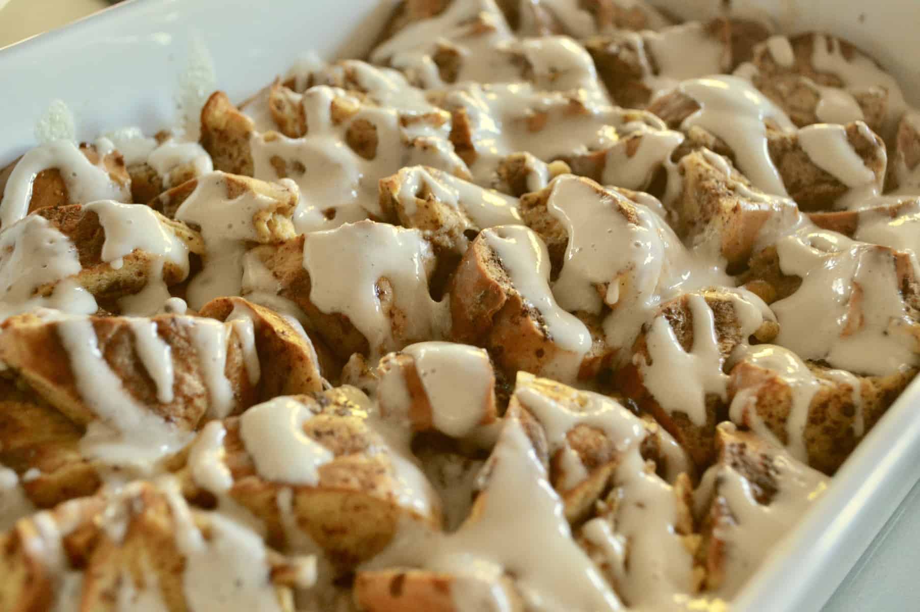 overnight bagel French toast in a white baking dish with maple cream cheese glaze 