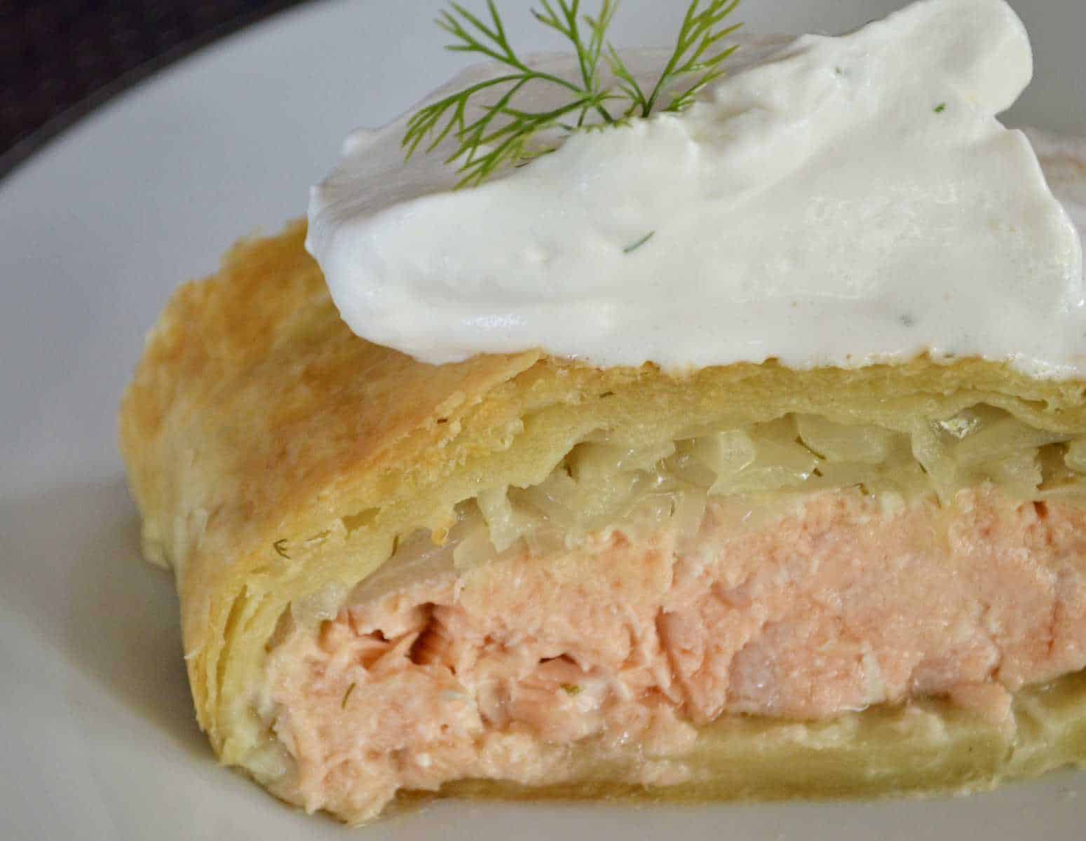 Salmon Wellington topped with caramelized onions, wrapped in puff pastry, and served with dijon dill cream sauce. 