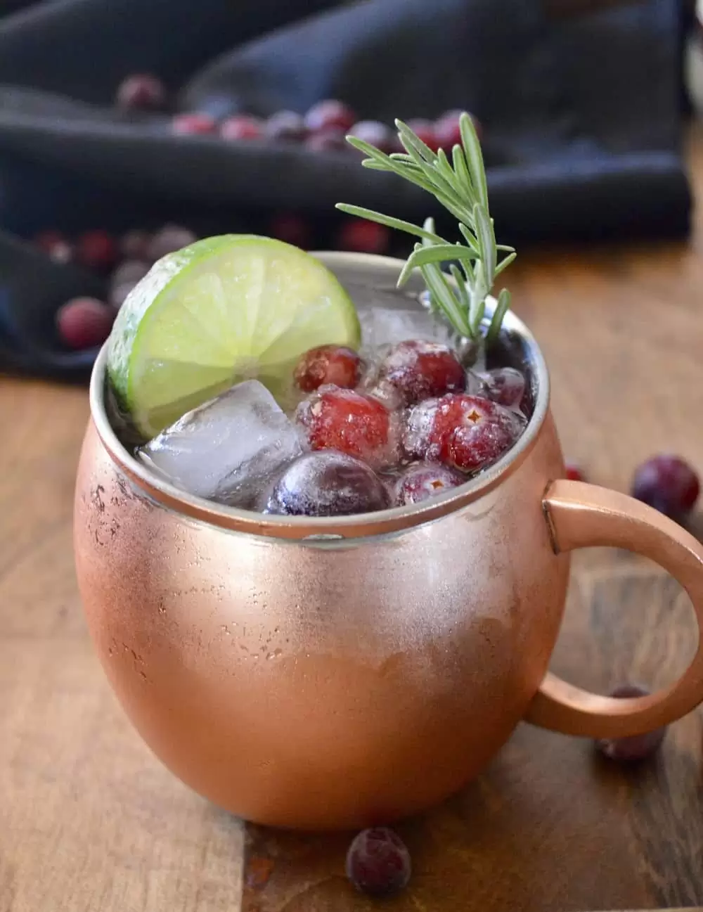 A copper coloured mug containing a mule cocktail, lime slice, cranberries and rosemary.