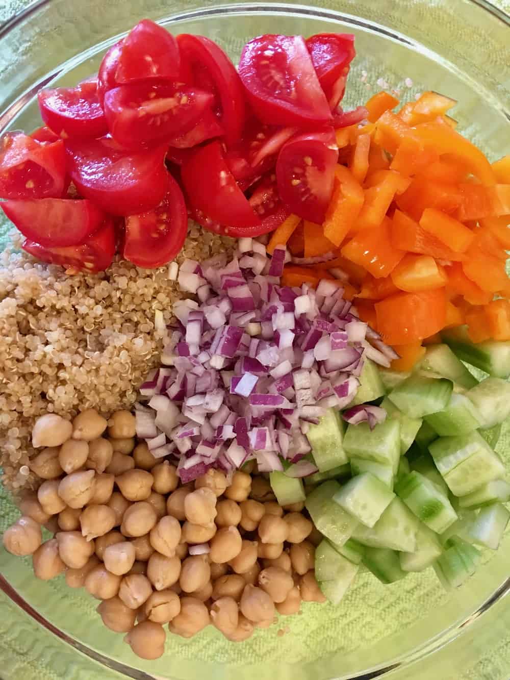 Bowl with quinoa, garbanzo beans, bell peppers, tomatoes, onions, and cucumbers. 