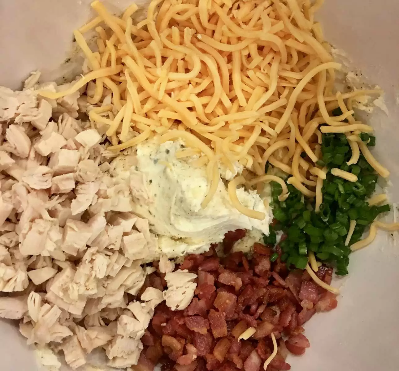 bowl of toppings including chicken, bacon, cheese, green onions, and cream cheese ranch dressing mix