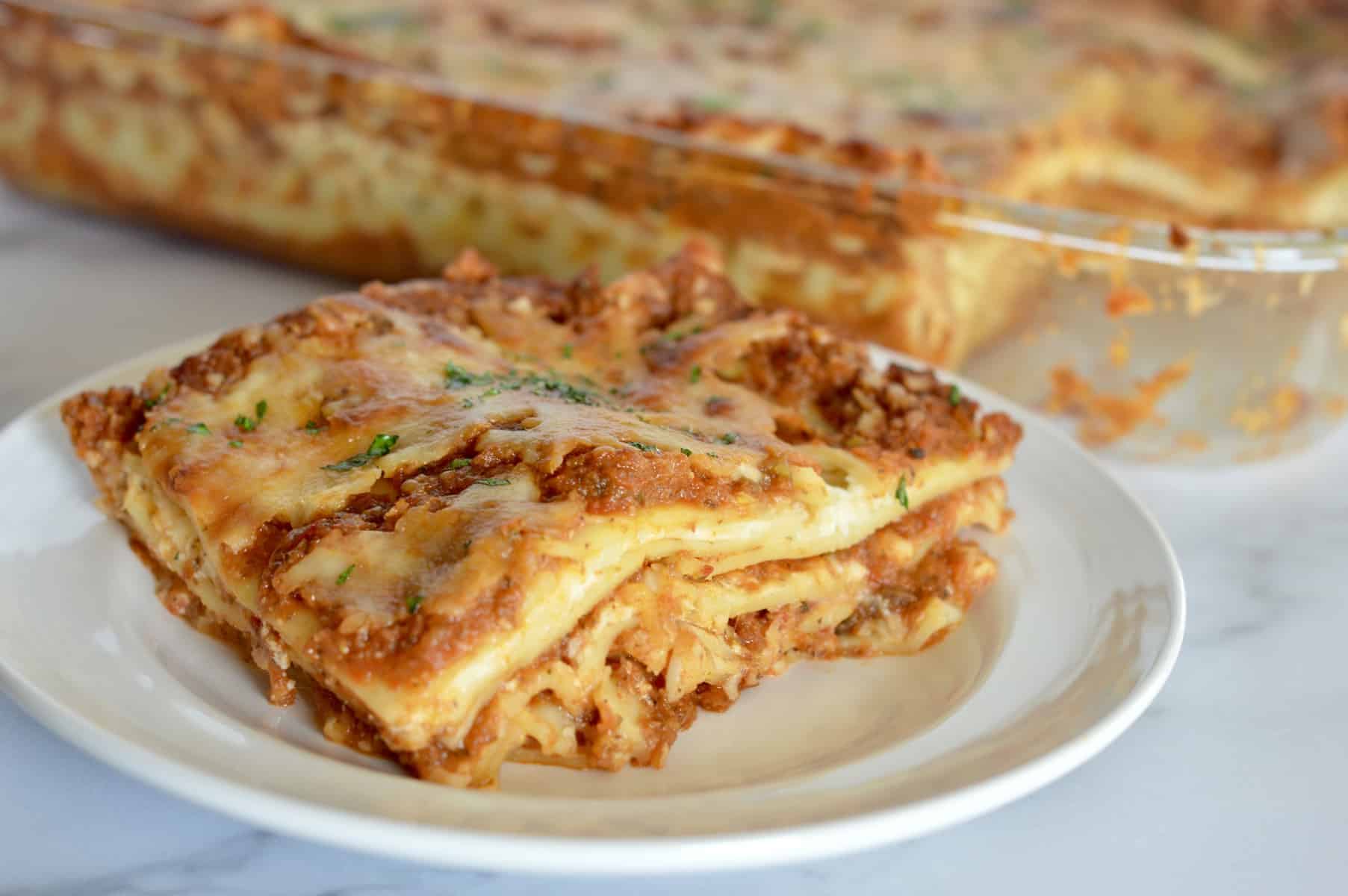 veggie lasagne on a white plate with a pan of it in the background 