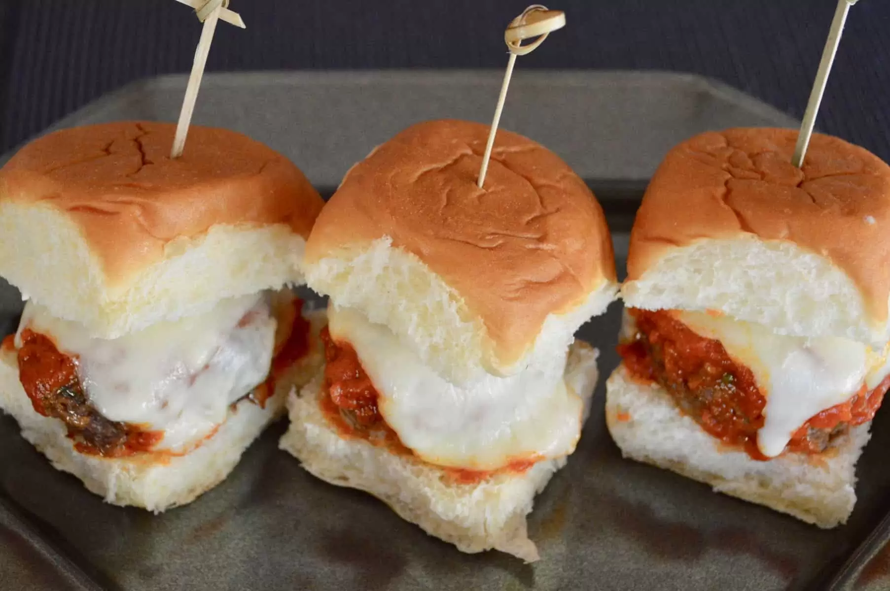 three Easy Italian meatball sliders on a plate with a bamboo stick in them 