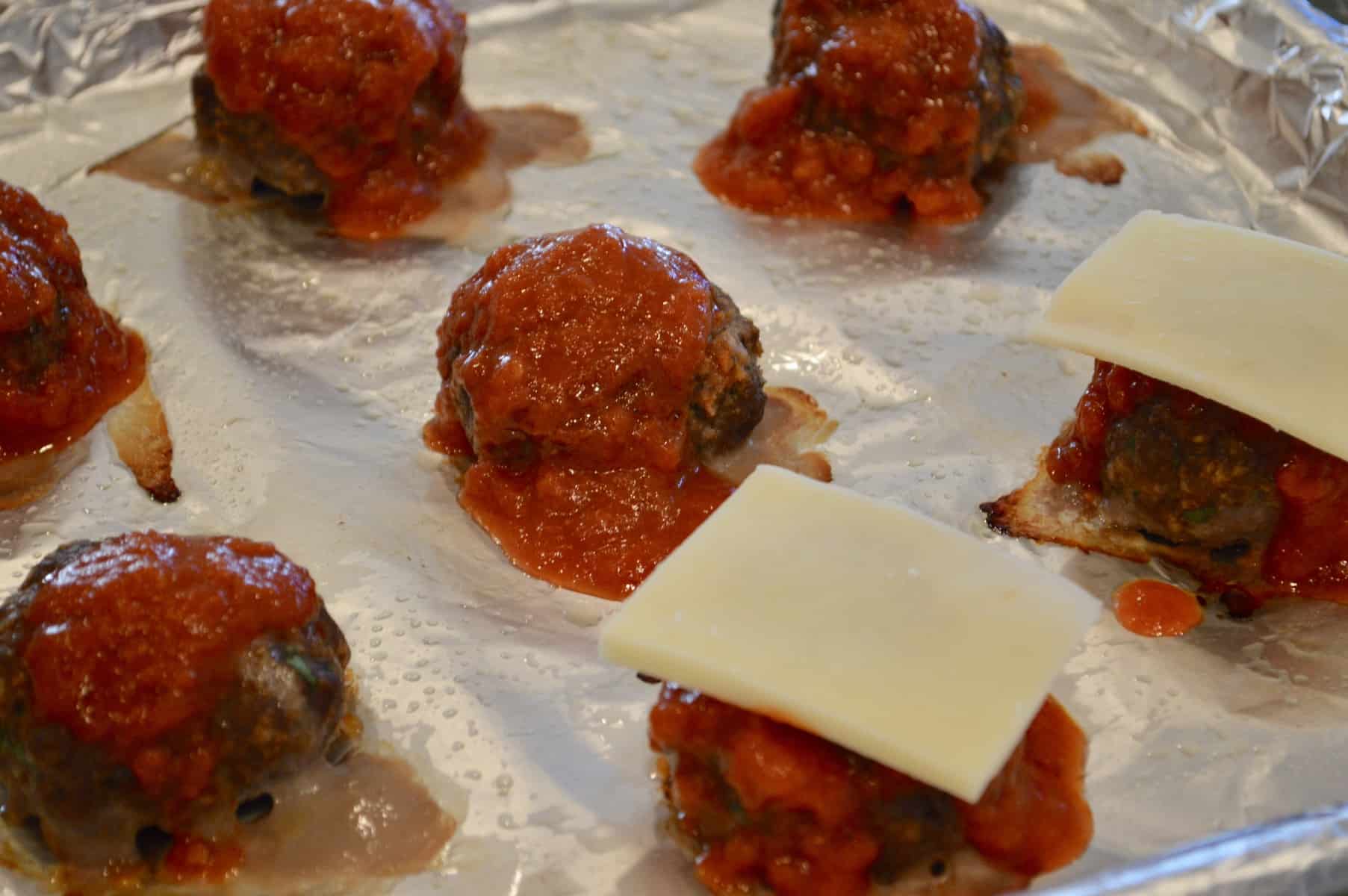 Easy Italian meatball sliders on a foil-lined baking sheet with sauce a mozzarella on top 