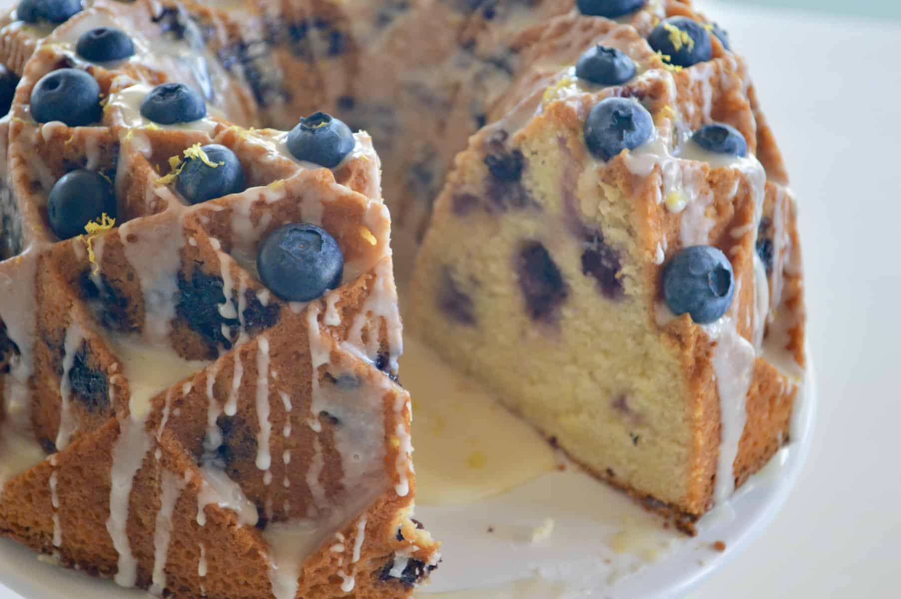 Blueberry Lemon Bundt Cake baked in a Jubilee Pan and garnished with blueberries and honey lemon drizzle