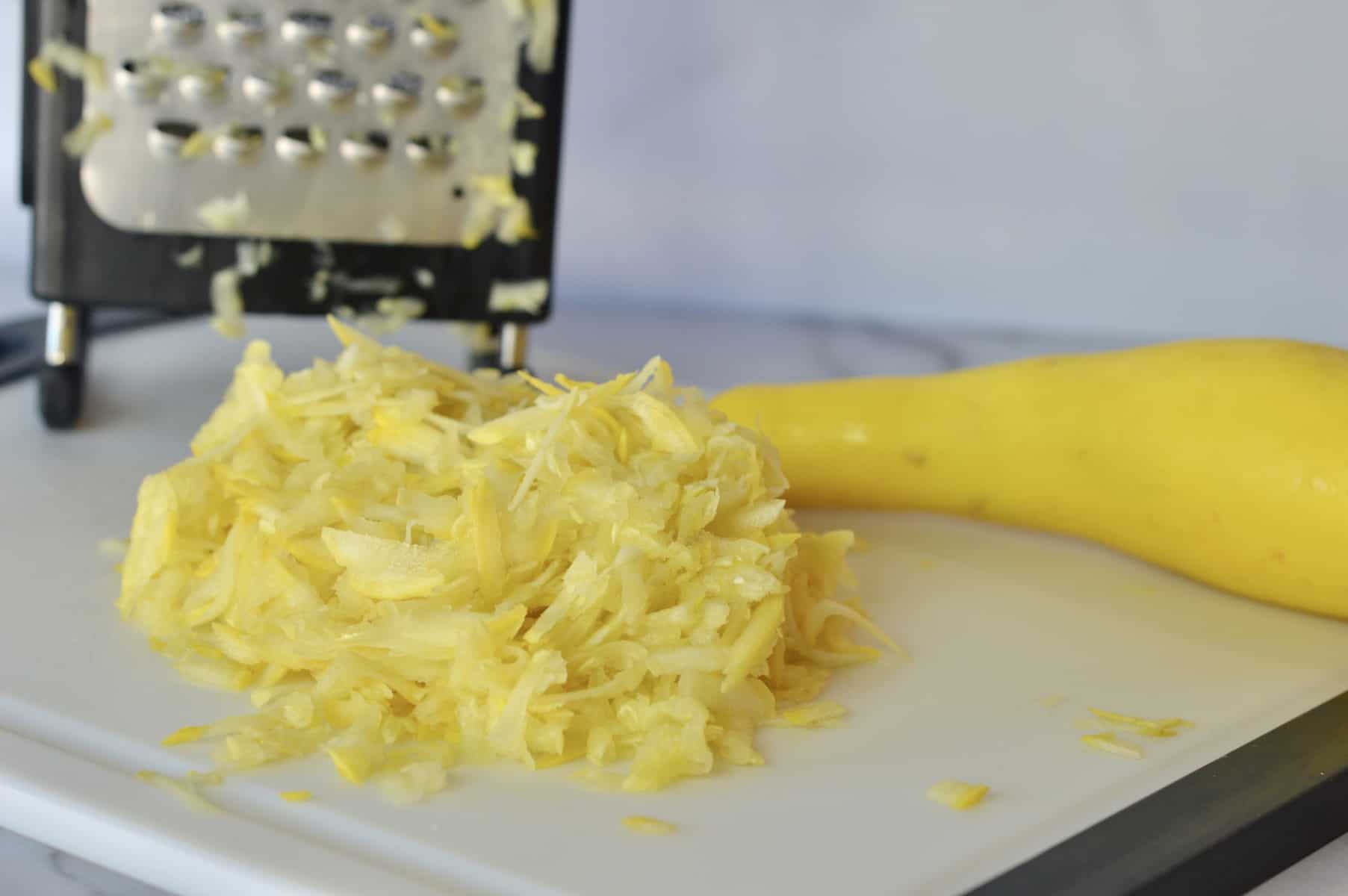 grated summer squash on a cutting board with box grater in the background 