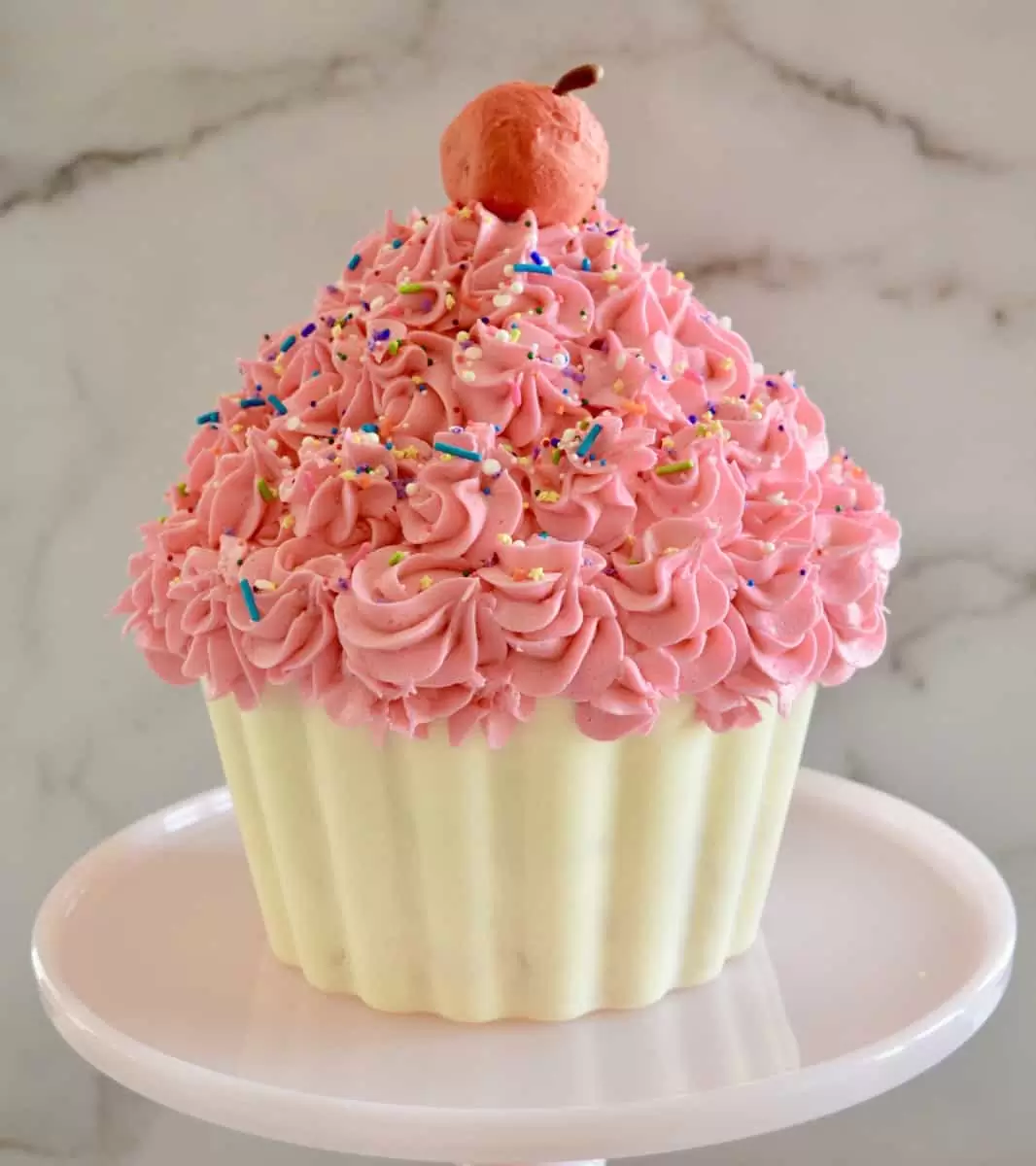 giant cupcake cake on a pink cake pedestal with a red cake truffle cherry on top