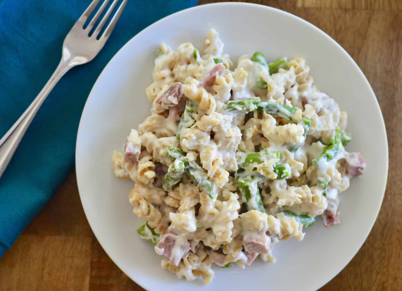 creamy ham and asparagus pasta on a white plate with green napkin and fork