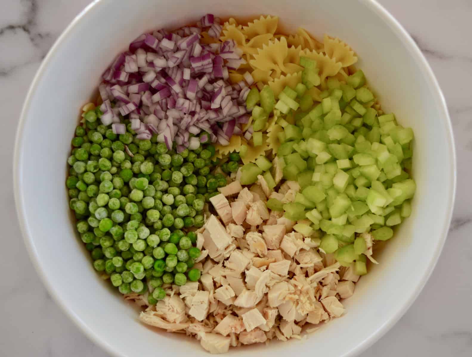 white bowl with pasta, celery, peas, and red onions. 