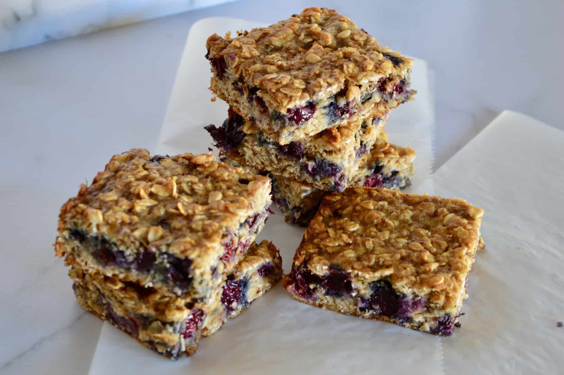 blueberry banana oat bars stacked on each other on a piece of white parchment paper 