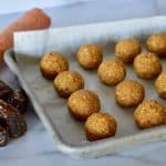 energy balls on a parchment lined baking sheet with dates and carrot in background