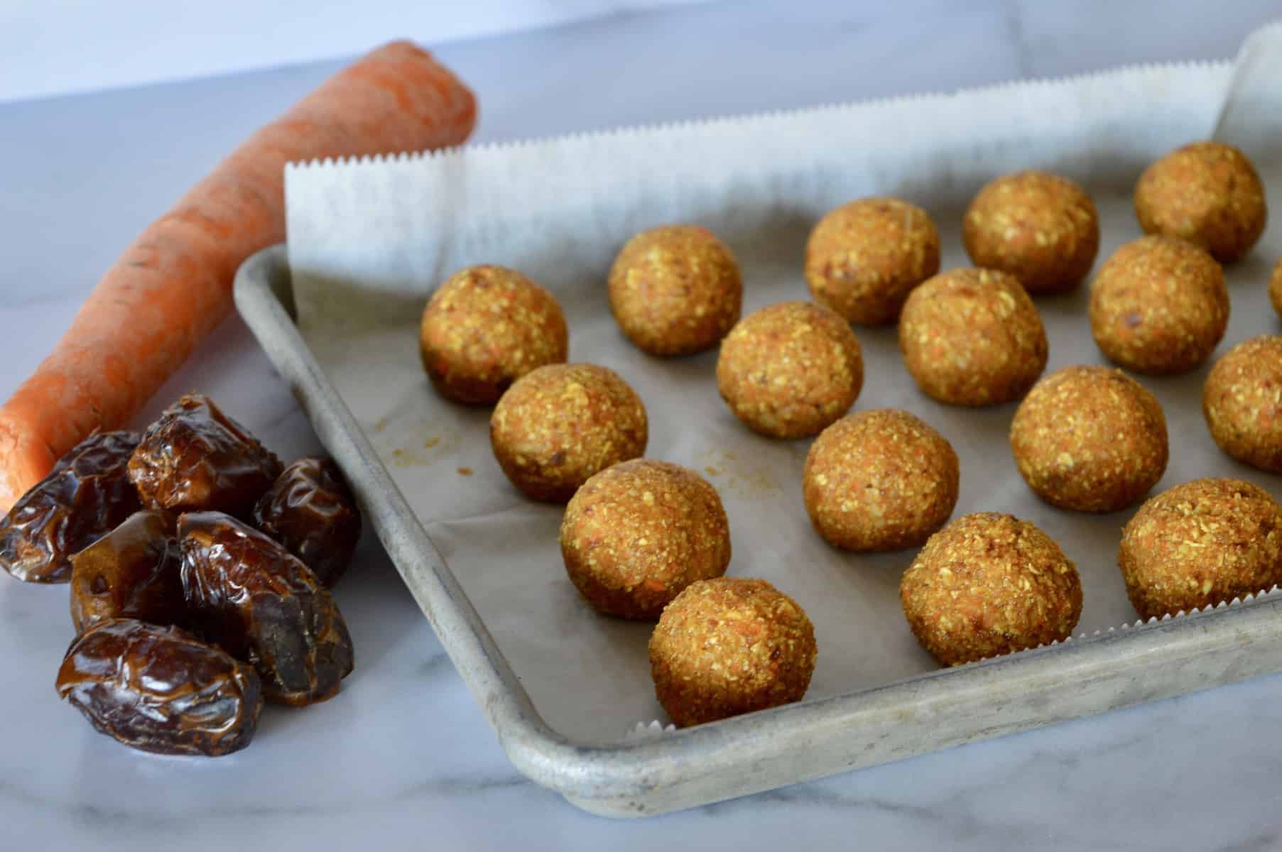 energy balls on a parchment lined baking sheet with dates and carrot in background 